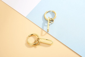 Detail of gold geometric hoop earrings with circular and bar pendants on colored background