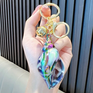 Chic iridescent gradient conch shell keychain with golden bell and ring on hand