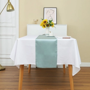 Detail of elegant teal satin table runner over a white tablecloth on a wooden dining table