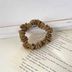 Close-up of khaki pleated satin hair scrunchie on vintage book page background