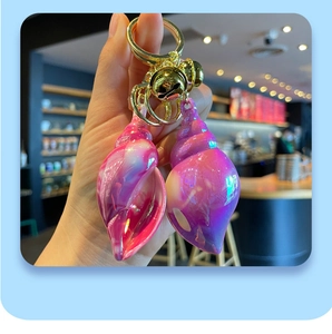 Handheld view of colorful iridescent acrylic conch keychains with gold bells and ring details