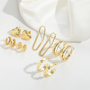 Detailed set of gold-plated hoop earrings and heart studs on white silk background