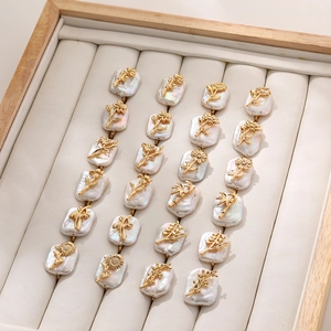 Golden flower earrings with baroque pearls arranged in a beige velvet jewelry tray