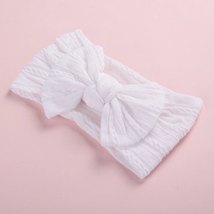 Close-up of white knitted nylon baby headband with large bow and cable knit texture
