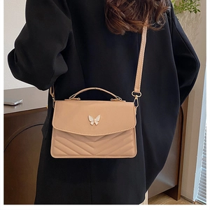 Detail of beige crossbody bag showing metal butterfly clasp and V-shape quilting on leather