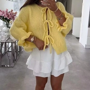 Detail of yellow tie-front knit cardigan paired with white ruffled skirt in a bright room