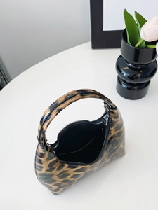 Glossy leopard print underarm handbag with zipper and top handle on a white table