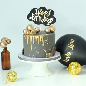 Macro shot of grey birthday cake featuring gold drip, spheres and Happy Birthday topper