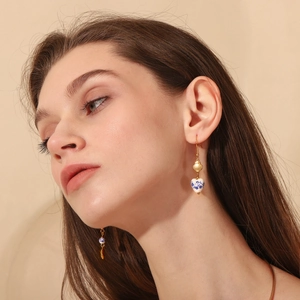 Detail shot of a heart-shaped blue and white porcelain earring with 18K gold hook