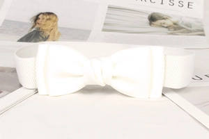 Detail view of a white elastic waist belt featuring a large decorative bow on a magazine