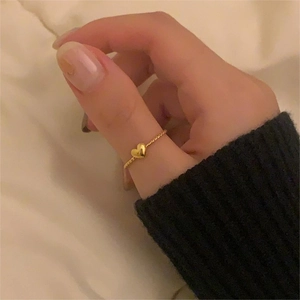 Close-up of a minimalist gold heart ring on finger with elegant warm fabric backdrop