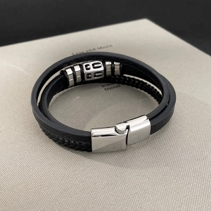 Macro detail of men's multi-layer leather bracelet with silver magnetic clasp and gear decor