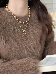 Detail of layered 18K gold plated necklace with tiger eye stone and pearls on a sweater