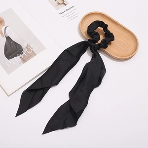Detail of elegant black satin hair scrunchie with long ribbon on a wooden tray