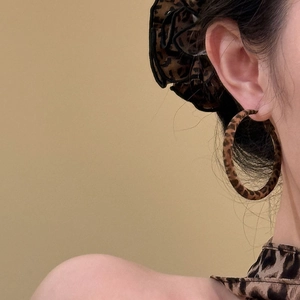 Close-up of a model wearing leopard print round hoop earrings in autumn brown