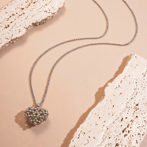 Détail du collier pendentif cœur argenté avec perles métalliques sur un support en pierre