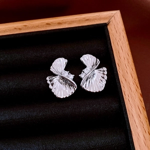 Close-up of silver shell-shaped earrings with zircon accents in a wooden jewelry box