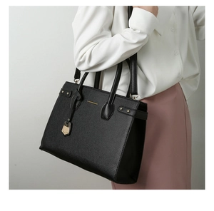 Close-up of black leather tote bag with gold logo and metallic pendant on a model