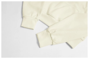 Detail of ribbed cuffs and hand pocket on a cream hooded sweatshirt with premium stitching