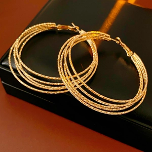 Close-up of golden multi-layer hoop earrings with textured finish on black leather box