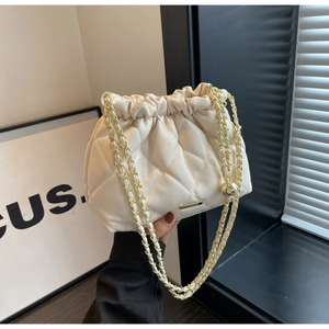 Detailed macro of cream quilted chain bag featuring golden hardware and drawstring closure