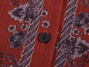 Macro view of floral print fabric with a black button on a red summer long dress