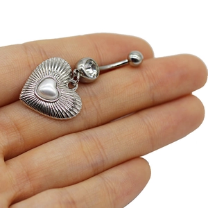 Macro shot of silver heart-shaped belly ring with white pearl and crystal zircon inlay