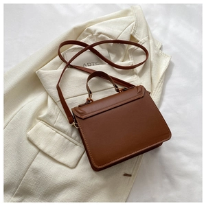 Brown PU leather square crossbody bag placed on a cream blazer for an elegant detail view