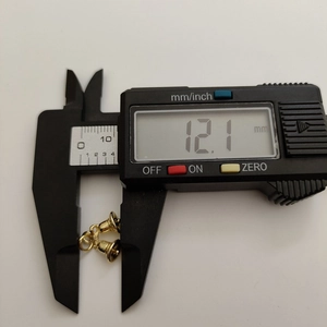Detailed measurement of 12.1 mm gold bell charm using a digital caliper tool