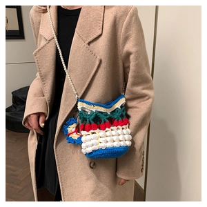 Detail of crochet bucket bag with cherry motifs and pearl strap on wool coat