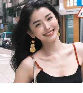 Close-up of golden geometric nested circle drop earrings worn by a smiling model