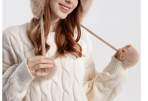Detail of beige knit winter hat with cable patterns, plush pom-poms and tie straps