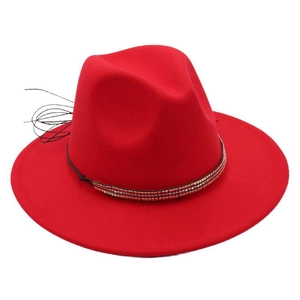 Détail d'un chapeau fedora rouge avec chaîne de perles dorées et plume noire élégante