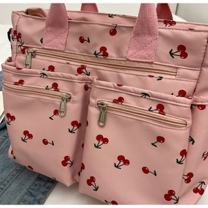 Pink tote bag detail with red cherry print featuring multiple front zipper pockets