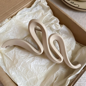 Detail view of a large wavy acrylic hair claw in beige placed in a premium gift box