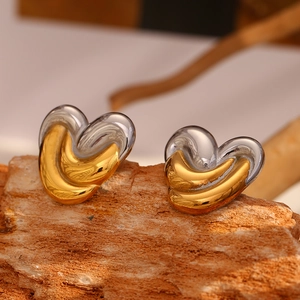 Macro detail of two-tone gold and silver heart stud earrings on a natural wood surface