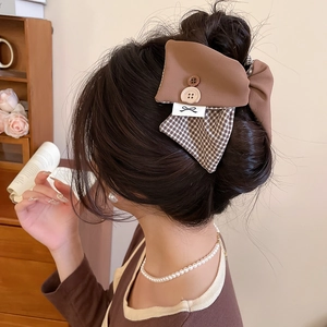 Detailed back view of a brown plaid bow hair clip with button detail on a model's hair