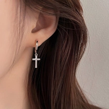 Close-up of a silver cross pendant hoop earring worn by a model in a punk hip-hop style