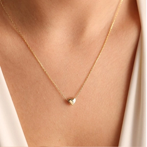 Close-up of minimalist gold heart pendant necklace on neck showing mirror polish texture