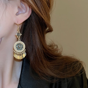 Detail of bohemian gold tassel earrings with blue stones and pearls on a model