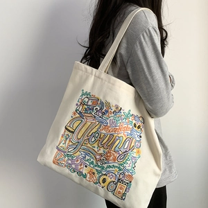 Detail of artistic embroidery on a cream canvas tote bag worn by a model on shoulder