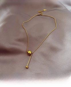 Detailed macro view of gold snake chain with minimalist solid gold ball and bar pendant
