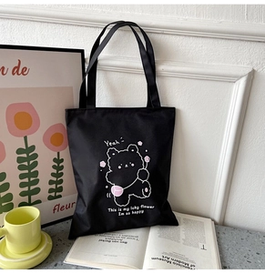 Close-up of black canvas tote bag with cartoon bear and floral pattern in lifestyle setting