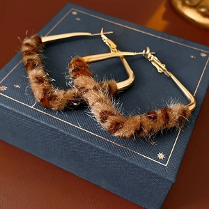 Dettaglio degli orecchini geometrici in metallo dorato con stampa leopardata in peluche