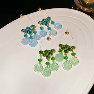 Elegant gold flower tassel earrings with blue and green crystals on white ceramic tray