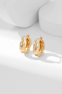 Detailed view of gold hoop earrings with star engravings and inlaid zircon gemstones