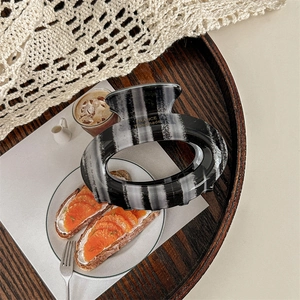 Detail of a large oval hair claw with black and grey stripes on a wooden tray