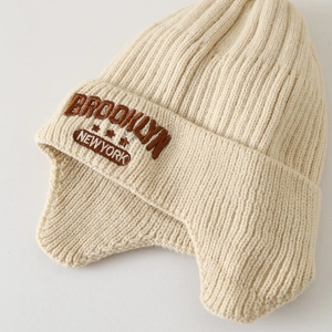 Dettaglio del berretto in maglia beige con ricamo Brooklyn e trama calda invernale