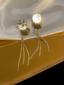 Detail shot of golden sequin tassel earrings with metallic finish on white silk background