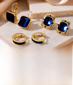 Detail of vacuum plated gold earrings with square blue zircons on a silk background